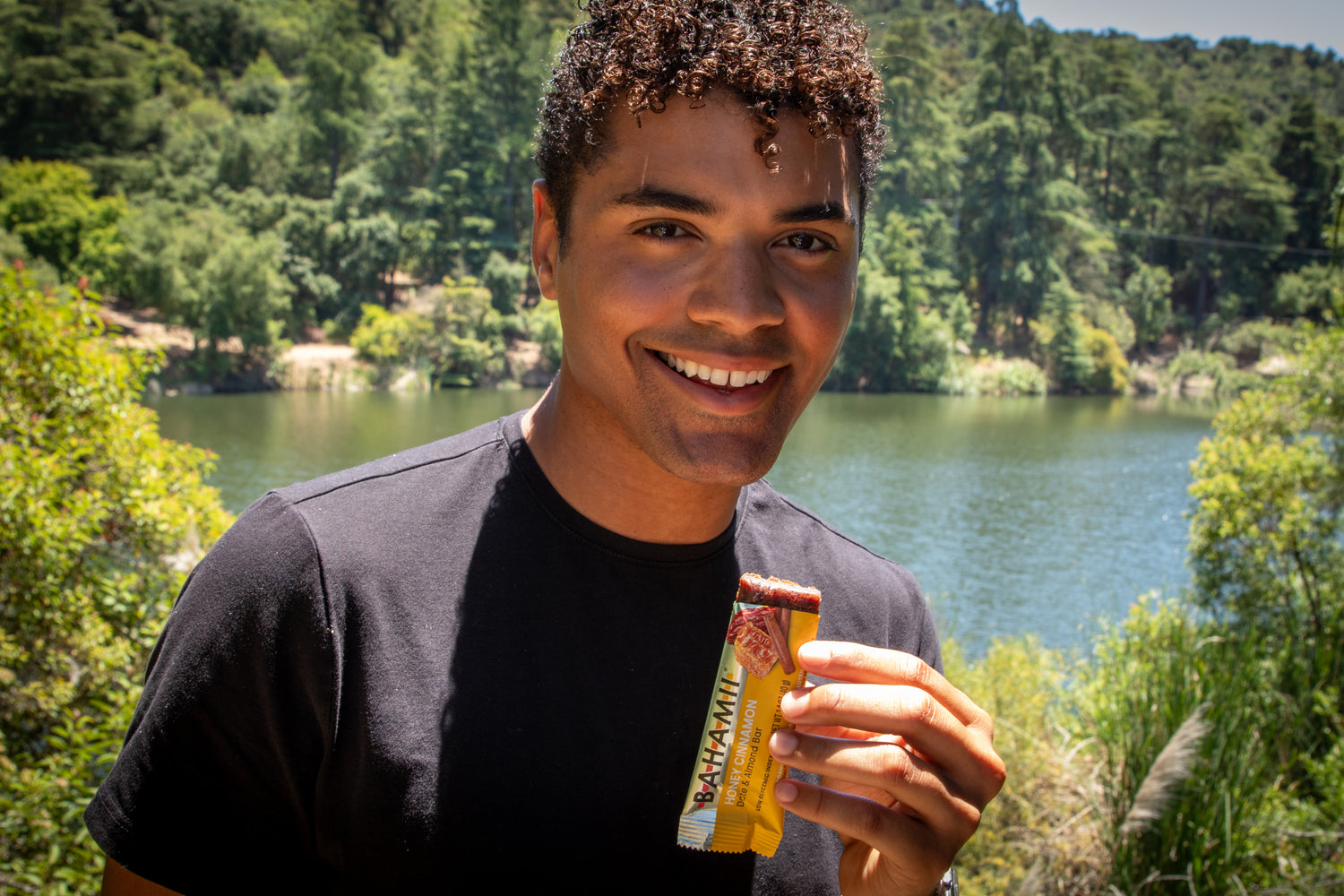 man holding Bahami honey cinnamon snack bar outdoors by lake