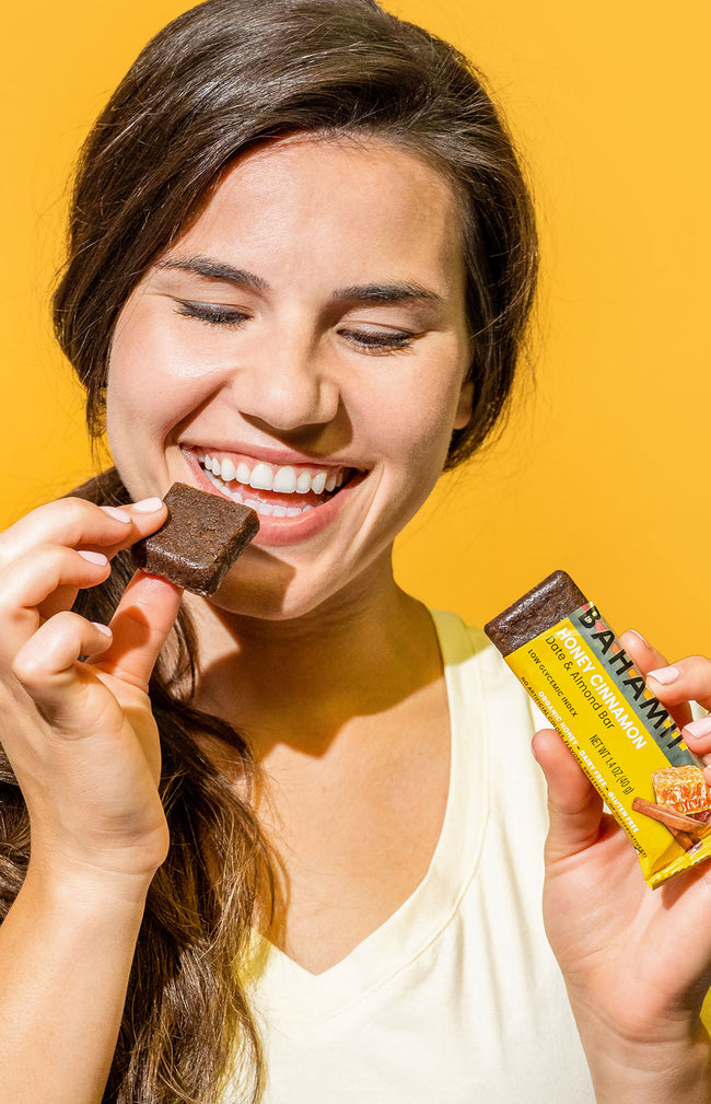 woman eating BAHAMII honey cinnamon date almond bar yellow background
